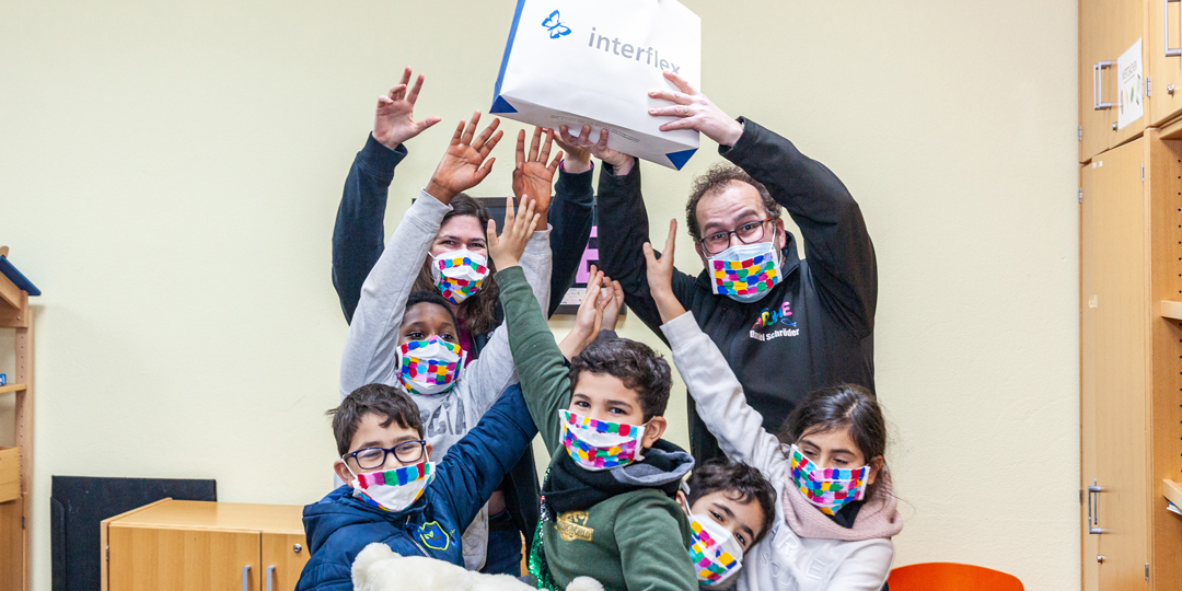 Gruppe von Kindern und Interflex-Mitarbeiterin bei Spenden-Übergabe an ARCHE Frankfurt