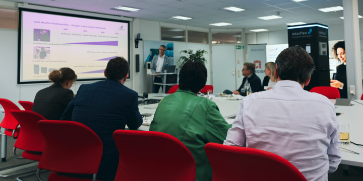 Mehrere Personen im Konferenzraum folgen einer Präsentation auf Leinwand