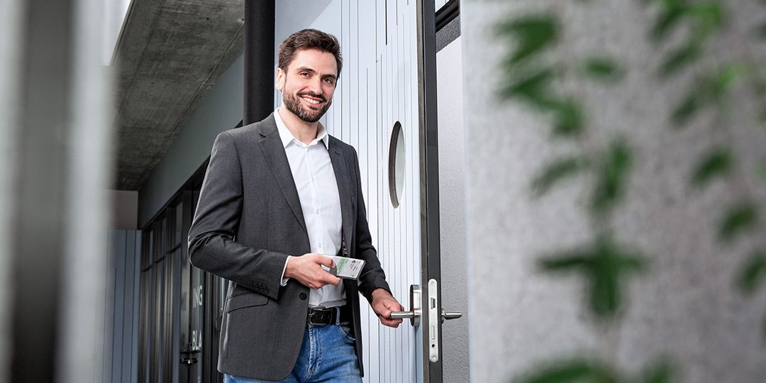 Un homme souriant ouvre la porte avec son smartphone grâce à la technologie Interflex-Opendor