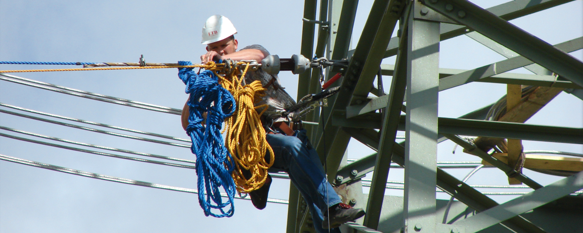 Arbeiter mit Schutzhelm führt Wartungsarbeiten an einem Strommast durch